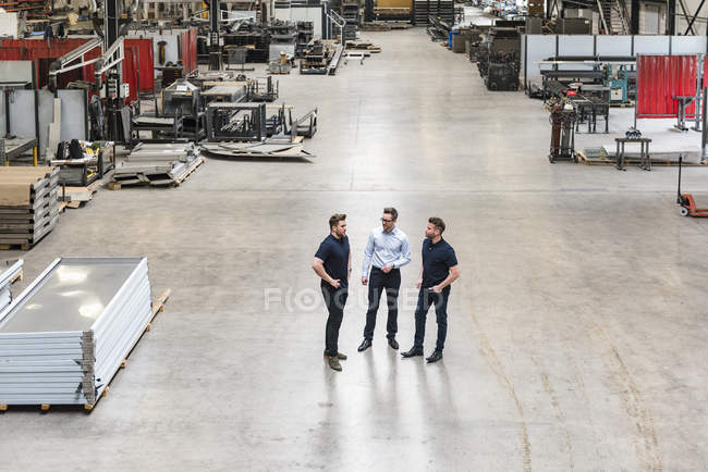 Tres hombres de pie y hablando en el piso de la fábrica - foto de stock
