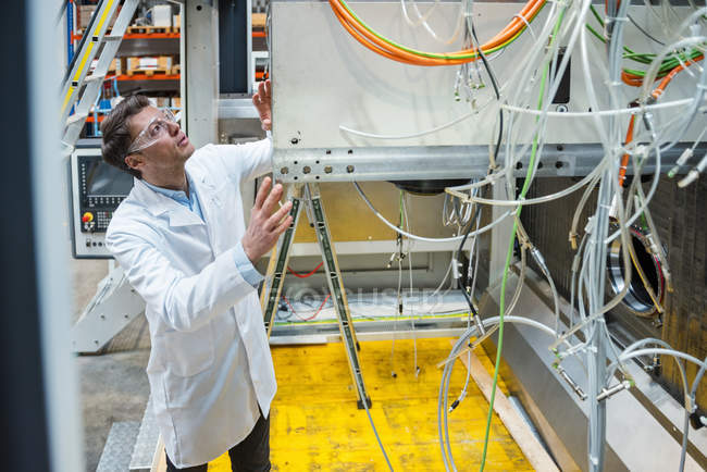 Man wearing lab coat and safety goggles examining at machine — Stock Photo