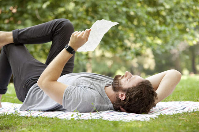 Мужчина лежит на одеяле в парке и читает письмо. — стоковое фото