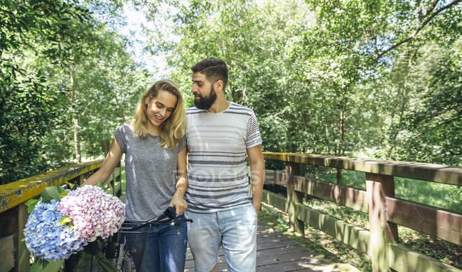 Casal andando em uma passarela de madeira com um buquê de hortênsias na cesta  de bicicleta — casuais, pessoas - Stock Photo | #263801548