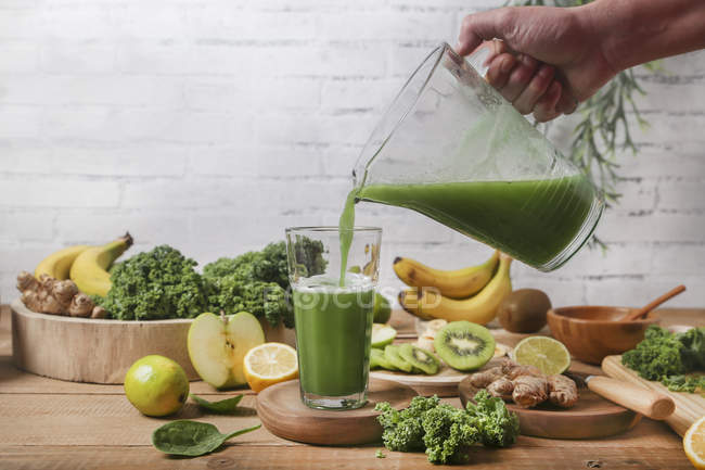 Man serving glass of green smoothie surrounded by ingredients — Stock Photo