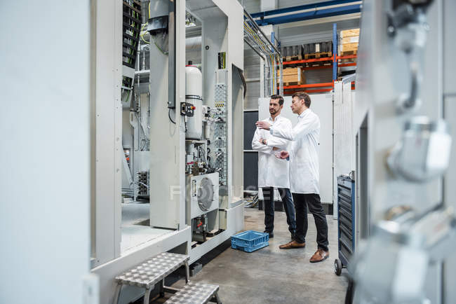 Two men wearing lab coats talking in factory — Stock Photo