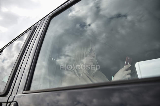 Junge Frau sitzt im Auto und schaut auf Handy — Stockfoto