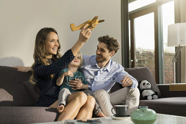 Pais felizes e filho brincando com avião de brinquedo de madeira no sofá em casa — Fotografia de Stock