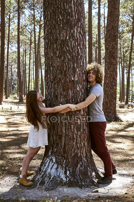 Feliz pareja joven abrazando el árbol en el bosque - foto de stock