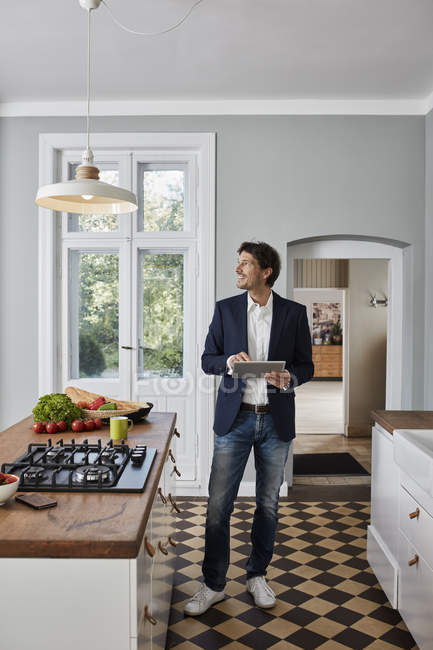 Man using tablet in kitchen and looking at ceiling lamp — Stock Photo