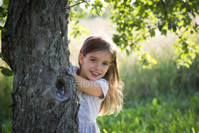 Young girl behind tree trunk at summer evening — Stock Photo