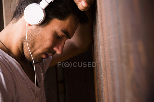 Serious young man wearing headphones and leaning against wooden wall — Stock Photo