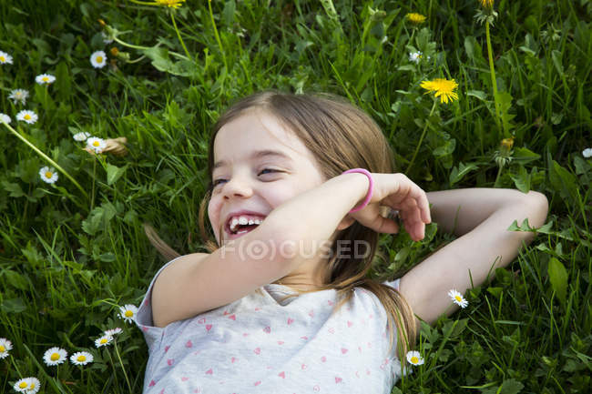 Portrait de petite fille riante allongée sur une prairie — Photo de stock