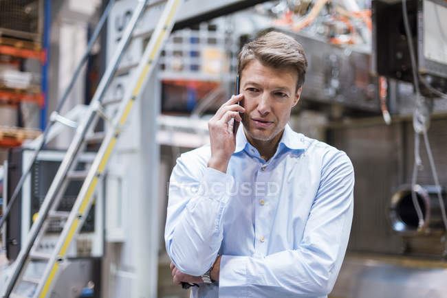 Businessman on cell phone in factory — Stock Photo