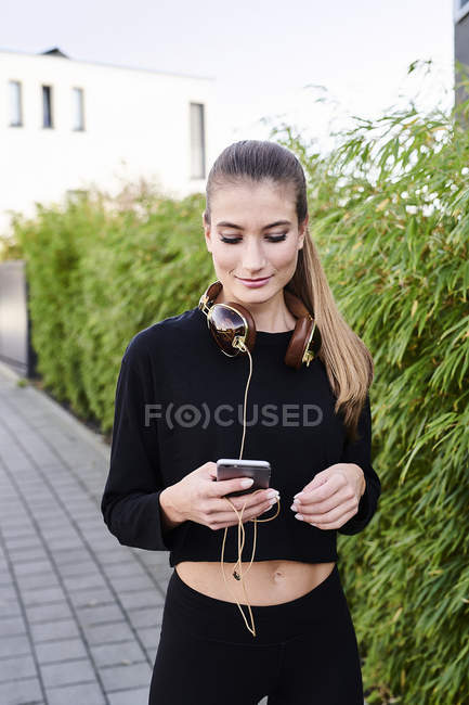 Sportive young woman with headphones and cell phone outdoors — Stock Photo
