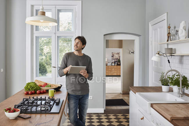 Hombre usando la tableta en la cocina y mirando a la lámpara de techo - foto de stock