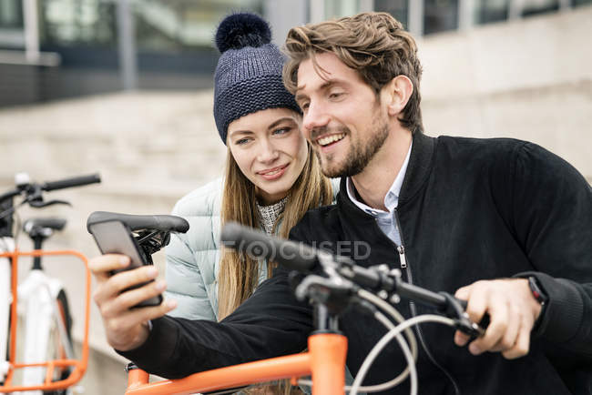 Pareja sonriente con bicicletas y teléfono celular en la ciudad - foto de stock