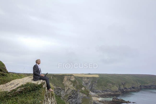 UK, Cornwall, Gwithian, businessman sitting at the coast and using laptop — Stock Photo