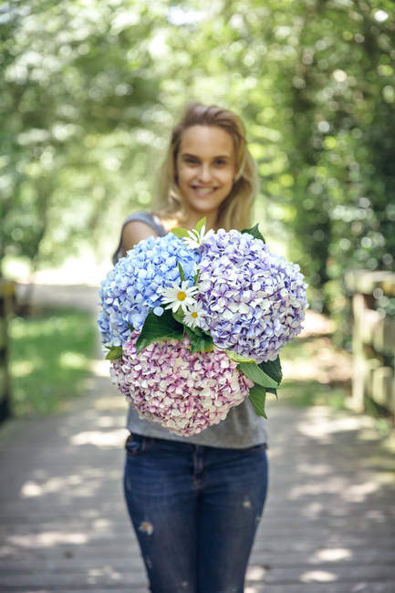Smiling young woman showing a bouquet of hydrangeas and daisies — Stock Photo