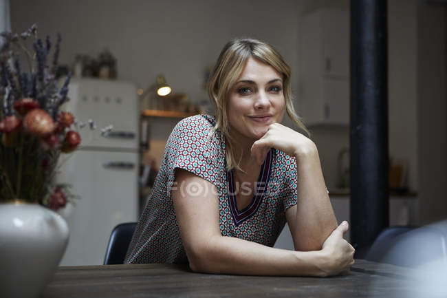 Retrato de una mujer sonriente sentada a la mesa en la cocina - foto de stock