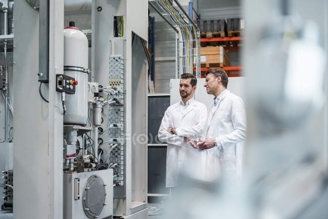 Two men wearing lab coats in factory looking at machine — Stock Photo