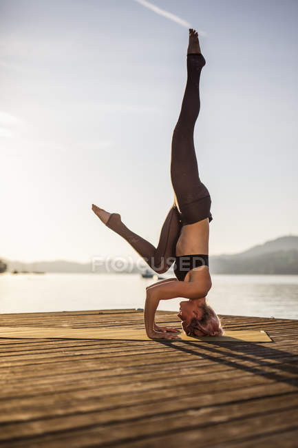 Mulher praticando ioga no molhe no lago e fazendo headstand — Fotografia de Stock