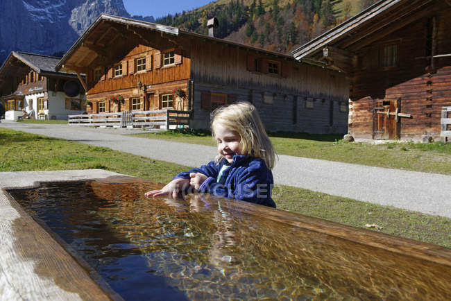 Austria, Tyrol, Eng, small girl bathing hand in drinking trough — Stock Photo