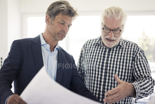 Man in suit and senior man looking at blueprint — Stock Photo
