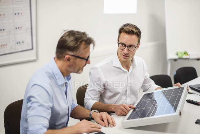 Два бизнесмена рассматривают солнечную панель на столе в офисе — стоковое фото