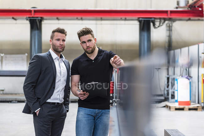Dos hombres con portapapeles hablando en el piso de la fábrica - foto de stock