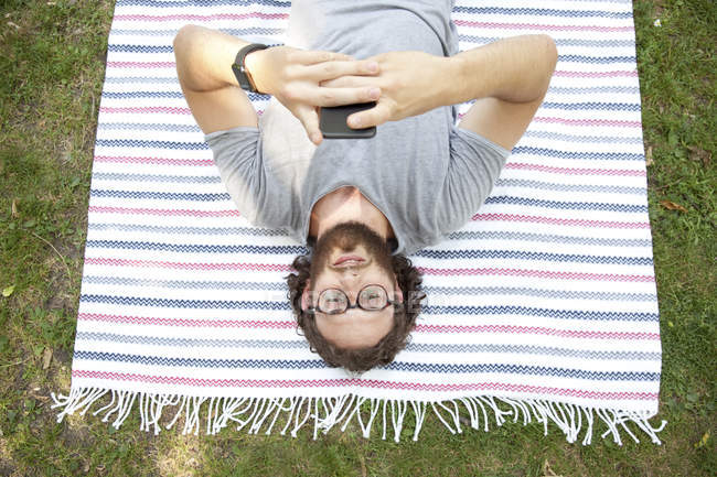 Людина лежав на ковдру в парку за допомогою мобільного телефону, вид зверху — стокове фото