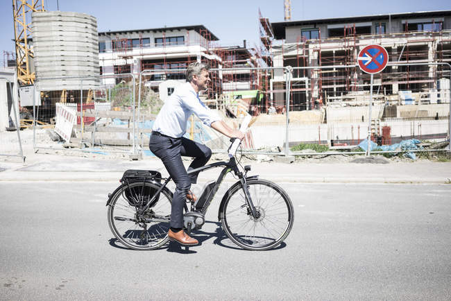 Uomo sorridente in e-bike lungo il cantiere — Foto stock