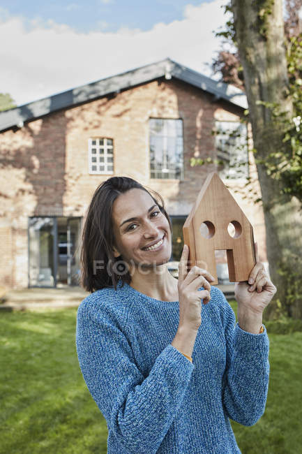 Portrait of smiling woman in garden of her home holding house model — Stock Photo
