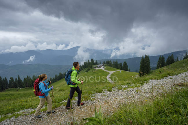 Germany, Lenggries, young couple with hiking poles hiking upwards ...