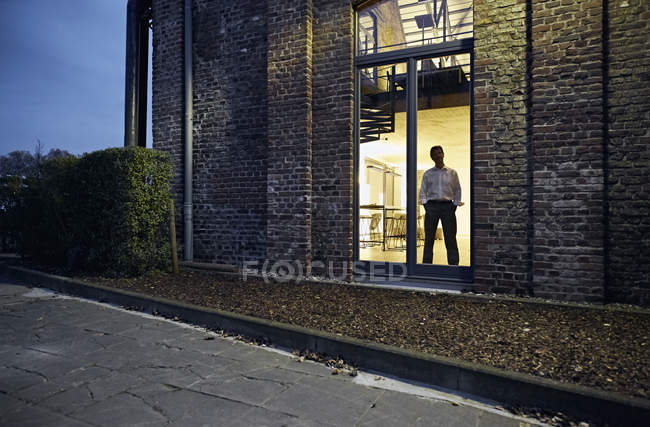 Vista exterior do homem em pé na janela do edifício moderno à noite — Fotografia de Stock