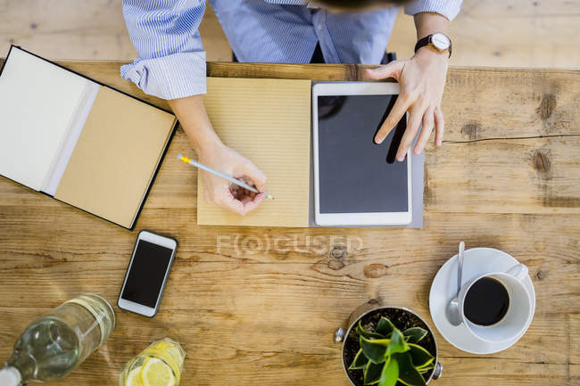 Vue du dessus de la femme au bureau en bois avec ordinateur portable, téléphone portable et tablette — Photo de stock