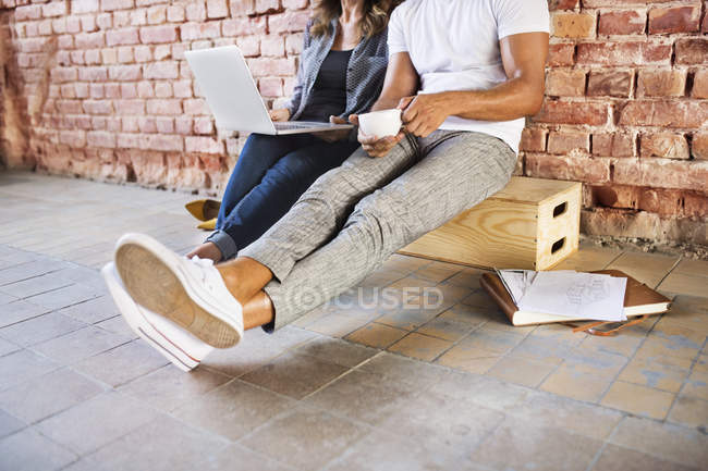 Empresario y mujer sentados en un loft, utilizando un ordenador portátil, fundando una empresa de nueva creación - foto de stock