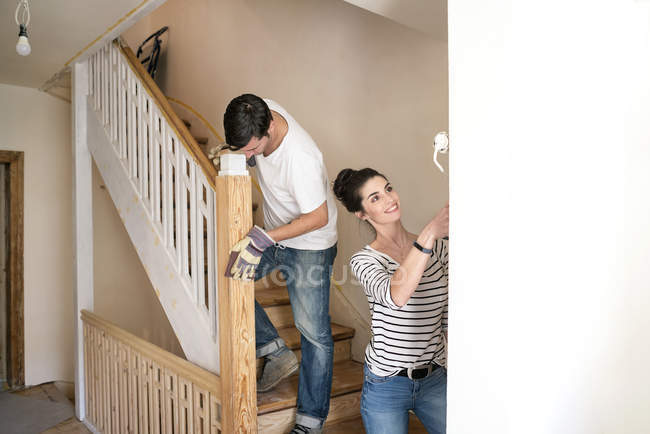 Pareja joven renovando nuevo hogar, pintando escalera - foto de stock