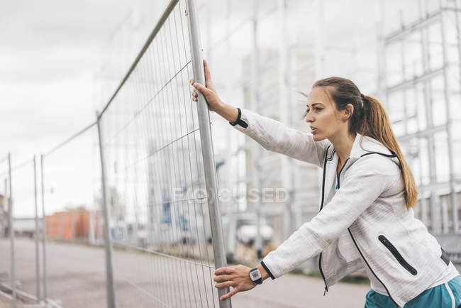 Sportive young woman standing at hoarding — Stock Photo