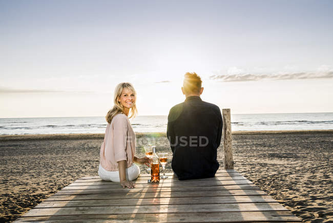 Coppia con bicchieri di vino seduti sul lungomare sulla spiaggia al tramonto — Foto stock