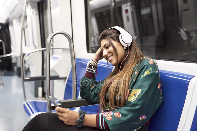 Sorrindo jovem ouvindo música com fones de ouvido e smartphone no trem subterrâneo — Fotografia de Stock