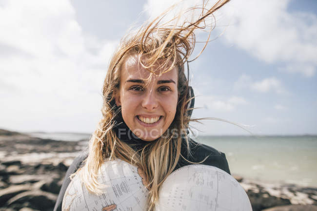 Francia, Bretaña, Landeda, retrato de una joven sonriente sosteniendo partes de un globo en la costa - foto de stock