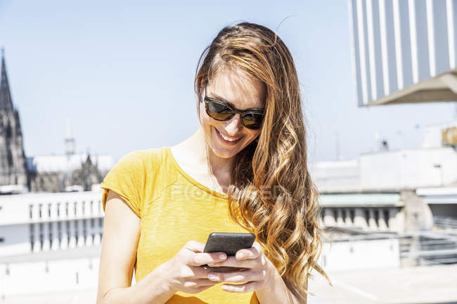 Alemanha, Colônia, mulher sorridente usando smartphone ao ar livre — Fotografia de Stock