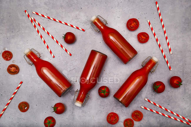 Homemade tomato juice in swing top bottles, straws and tomatoes on grey ground — Stock Photo
