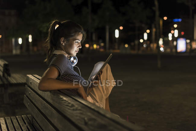 Young woman sitting on bench at night using tablet — Stock Photo