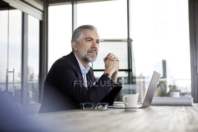 Uomo d'affari con computer portatile alla scrivania in ufficio pensando — Foto stock