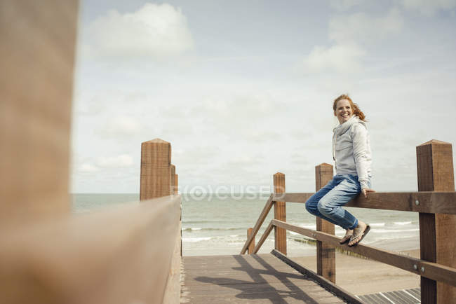 Femme assise sur une clôture à la mer, souriante — Photo de stock