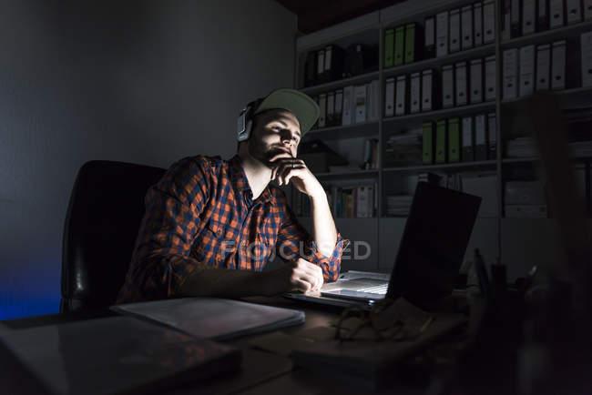 Ritratto di freelance seduto alla scrivania di notte con laptop e cuffie — Foto stock