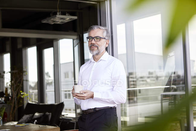 Бизнесмен, стоящий у французской двери с чашкой кофе — стоковое фото