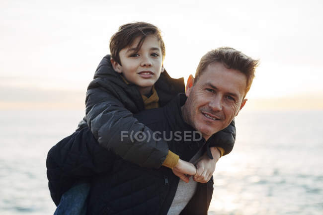 Vater gibt Sohn bei Sonnenuntergang Huckepack am Strand — Stockfoto