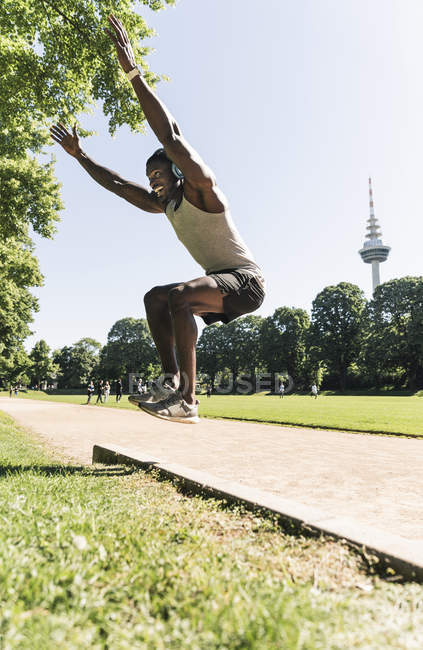 Atleta joven con auriculares, escuchar música, entrenamiento de salto largo - foto de stock