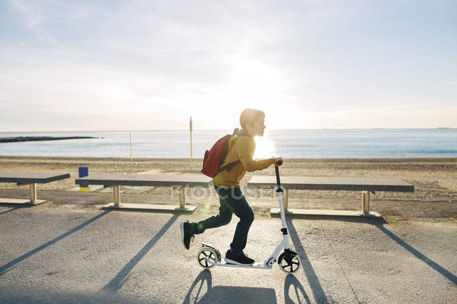 Junge fährt Roller auf Strandpromenade bei Sonnenuntergang — Stockfoto