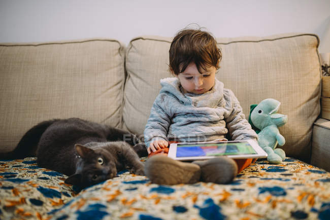 Babymädchen sitzt mit digitalem Tablet auf Couch bei Katze — Stockfoto