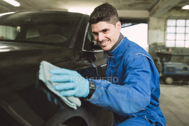 Hombre sonriente limpiando un coche en un taller - foto de stock
